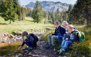 Nachhaltiges Reisen - Kinder an Bach in den Bergen der Schweiz